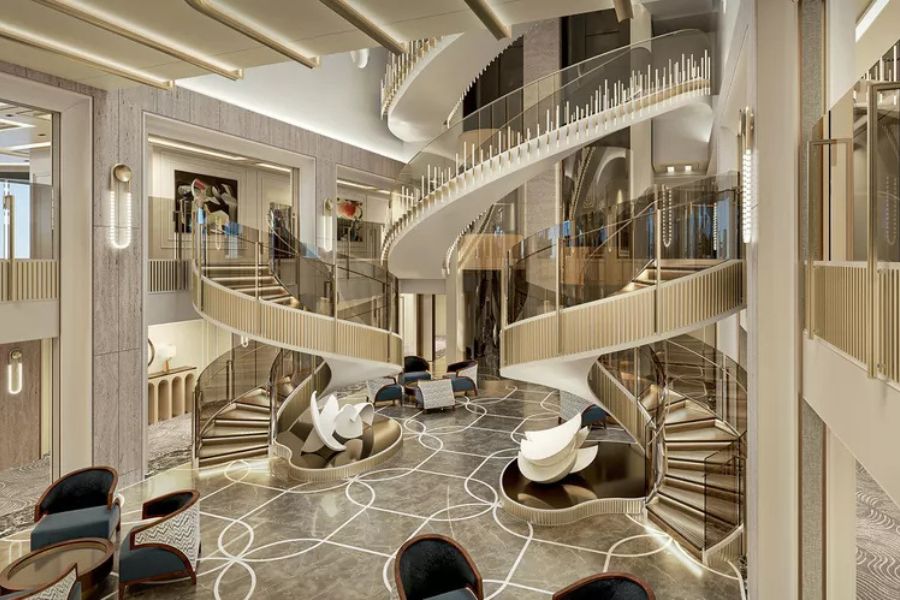 A bright modern cruise ship atrium has sweeping curved staircases rising through several levels. Glass railings sculptural white seating and patterned flooring create an upscale open interior.