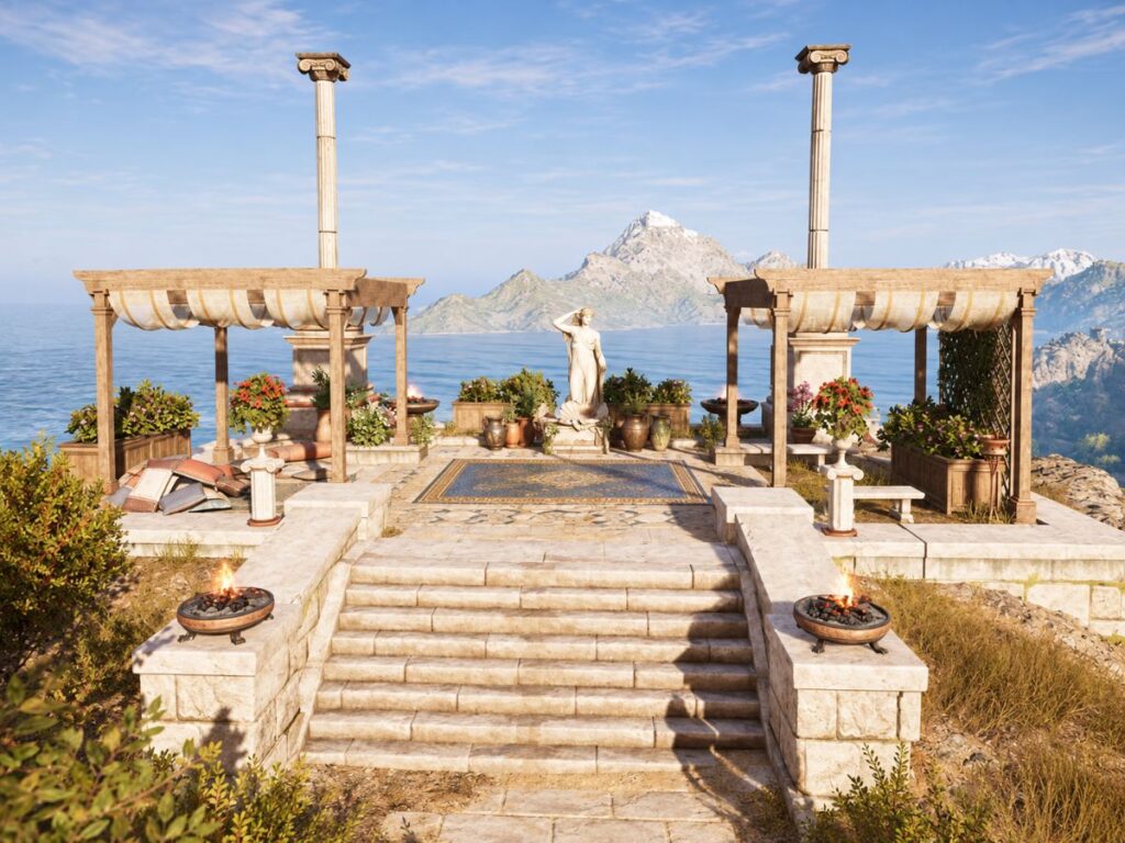 Classical style stone terrace overlooking a calm sea and dramatic mountain peaks. Tall columns frame a central statue with flowering plants and fire bowls arranged around the steps.