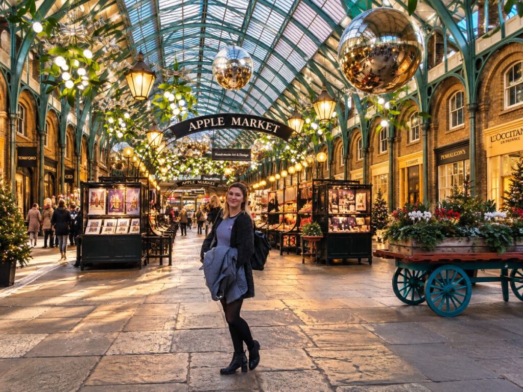 A woman poses inside Covent Garden Apple Market during Christmas in London. Giant silver baubles hang from the glass ceiling above festive market stalls decorated with glowing lights and greenery at one of the most popular London Christmas markets.
